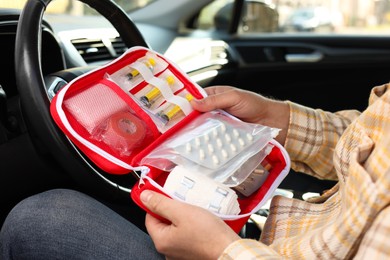 Photo of Man holding first aid kit with medicaments inside car, closeup