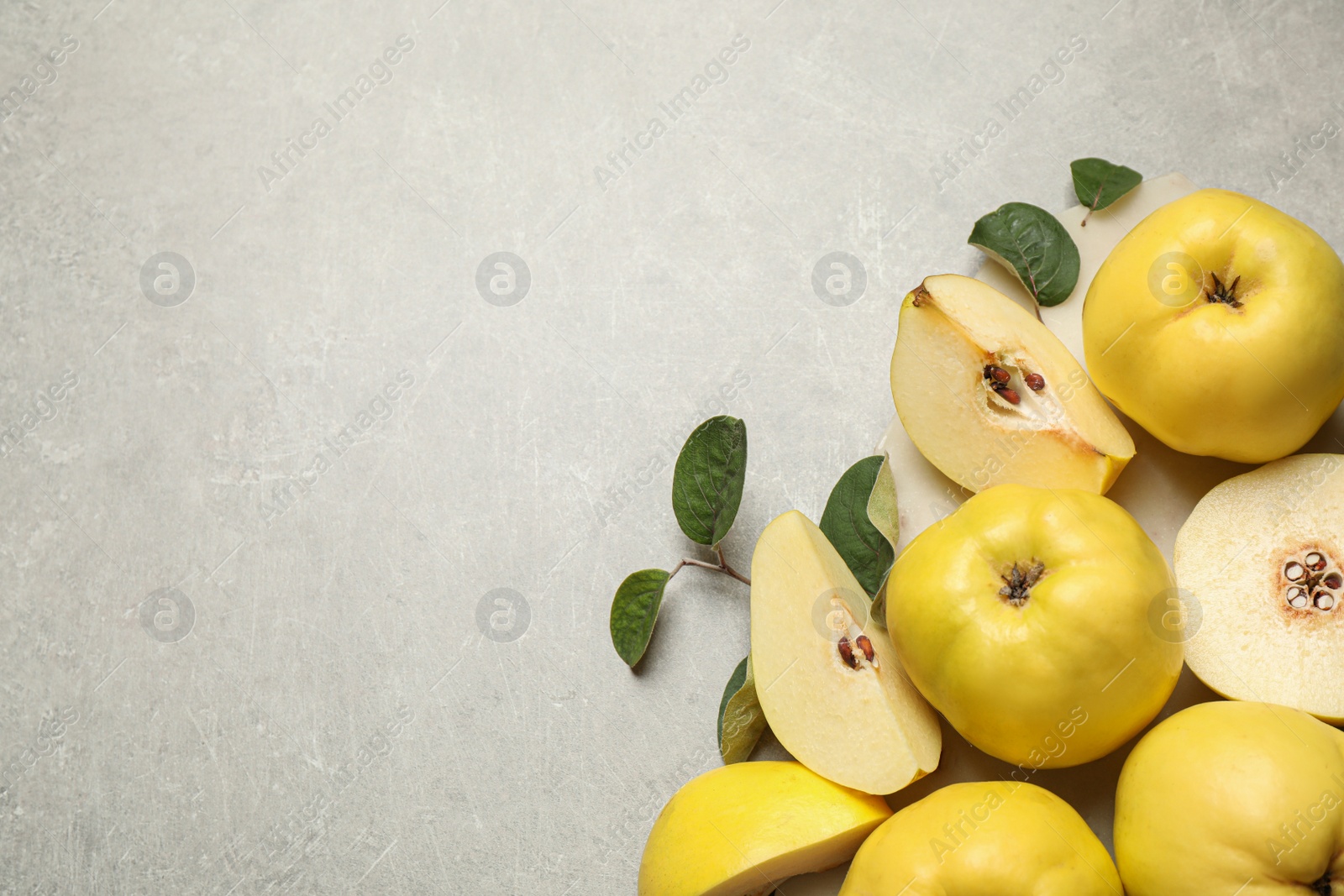 Photo of Fresh ripe organic quinces with leaves on grey table, flat lay. Space for text