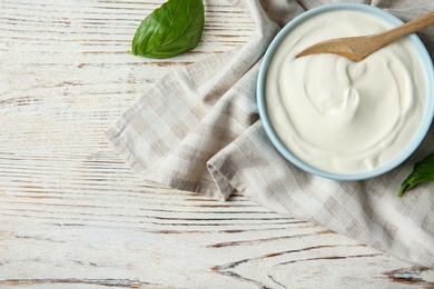 Photo of Bowl of sour cream with spoon and napkin on white wooden table, flat lay. Space for text