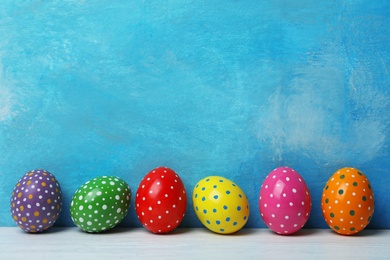 Decorated Easter eggs on table near color wall. Space for text