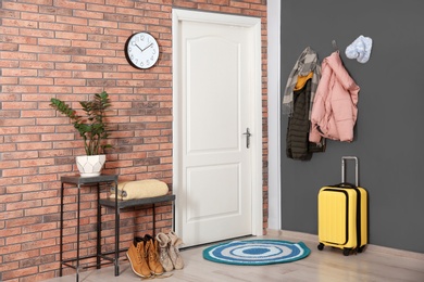 Modern hallway interior with stylish furniture, suitcase and clothes on wall