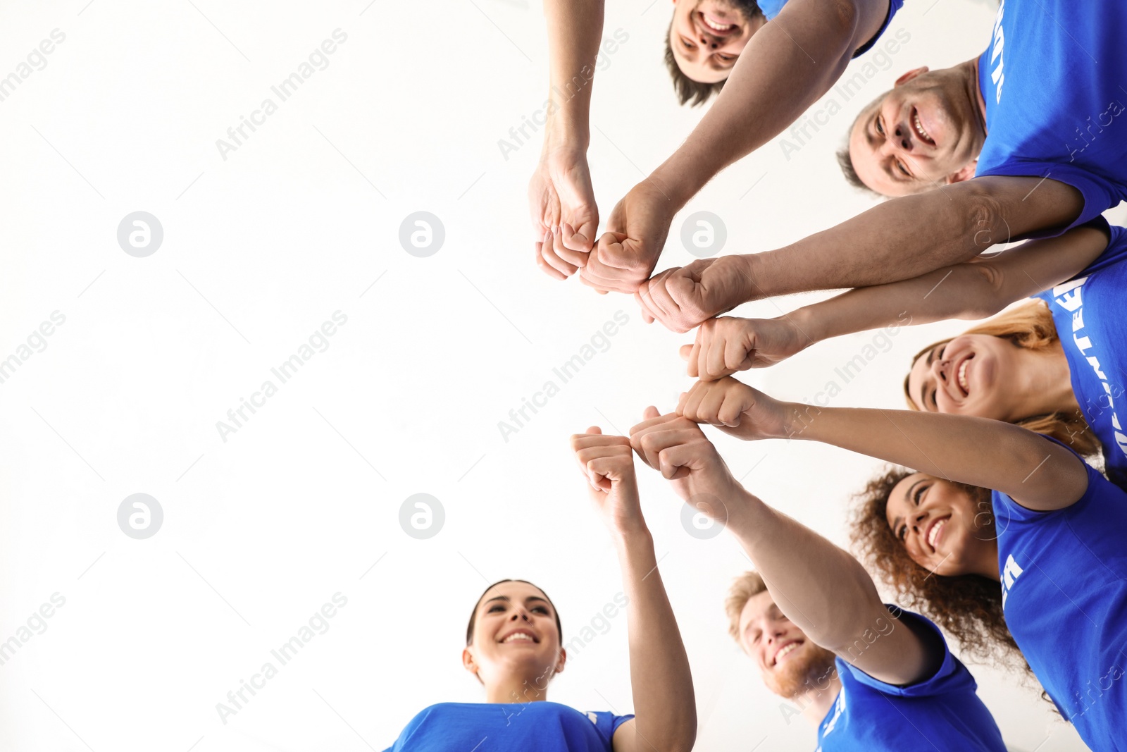Photo of Team of volunteers putting their hands together on light background, bottom view. Space for text