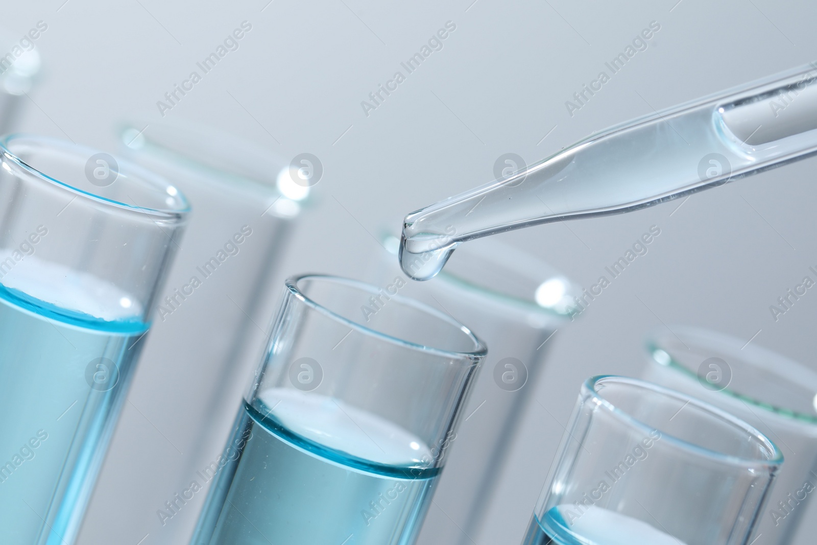 Photo of Dripping liquid from pipette into test tube on light background, closeup