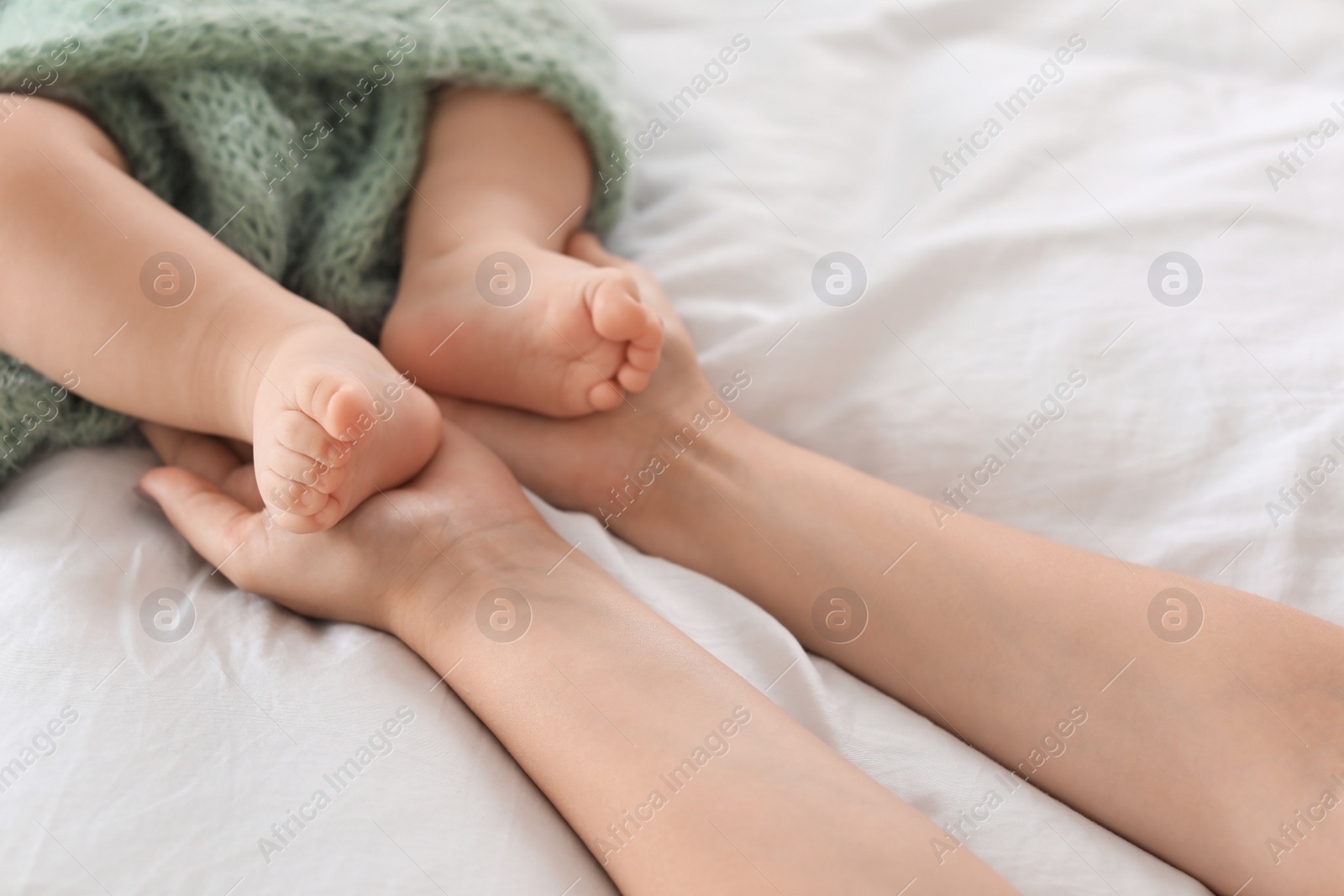 Photo of Mother holding feet of her little baby on bed, closeup
