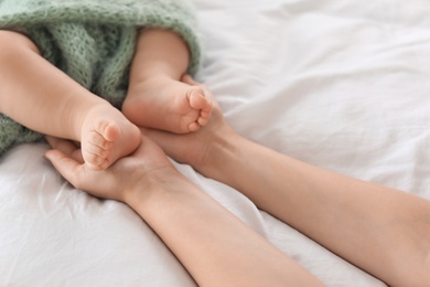 Photo of Mother holding feet of her little baby on bed, closeup