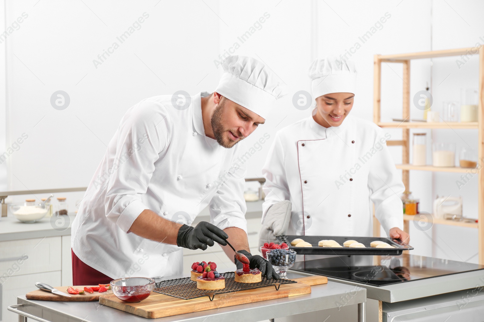 Photo of Pastry chefs preparing desserts at table in kitchen