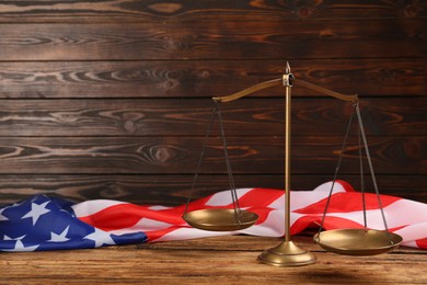 Photo of Scales of justice and American flag on wooden table. Space for text