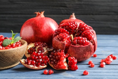 Photo of Bowl with seeds and ripe pomegranates on table against dark background