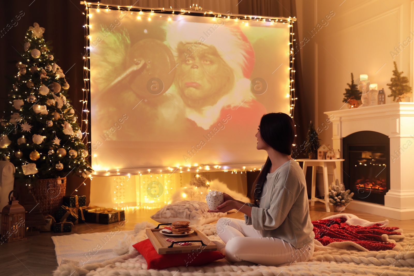 Photo of MYKOLAIV, UKRAINE - DECEMBER 24, 2020: Woman watching The Grinch movie via video projector in room. Cozy winter holidays atmosphere