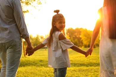 Photo of Little girl and her parents holding hands in park. Happy family