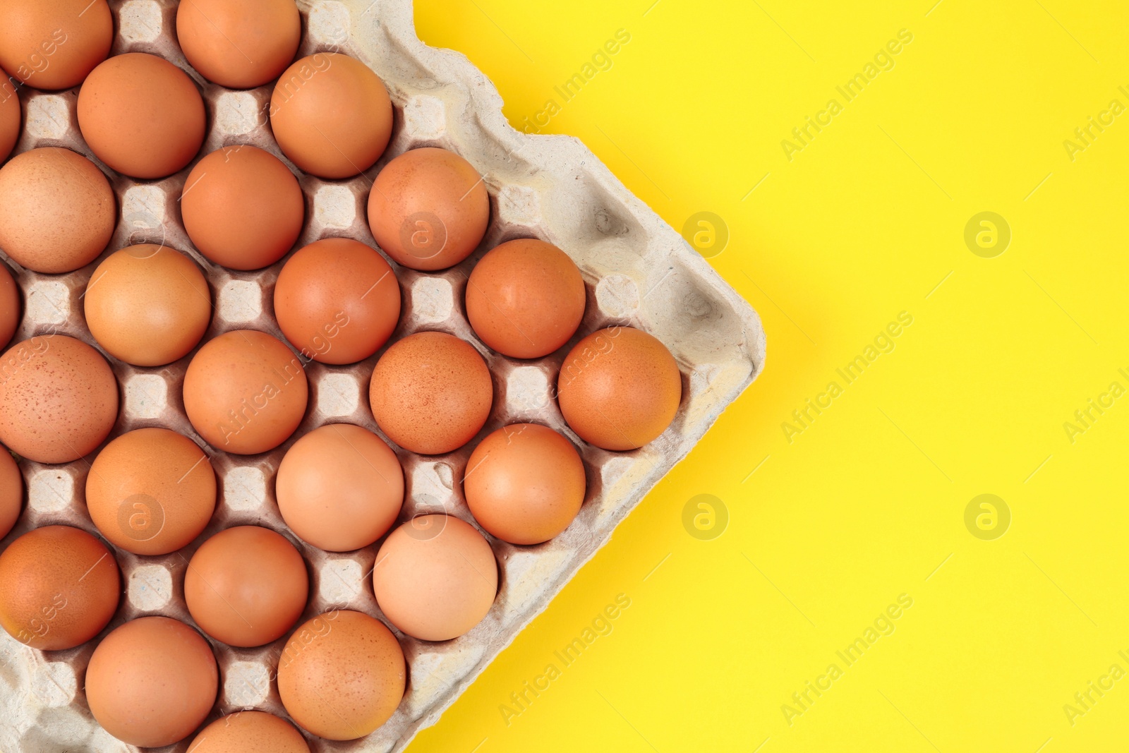 Photo of Raw chicken eggs on yellow background, top view