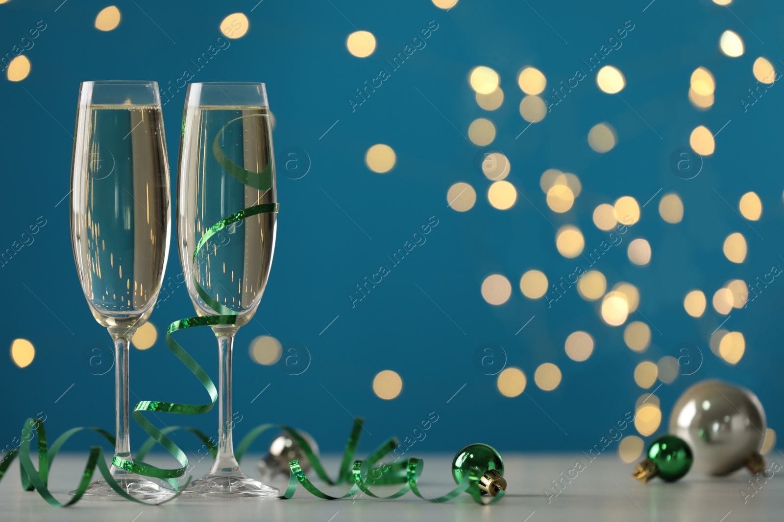 Photo of Glasses of champagne with serpentine streamers and Christmas balls on table against blurred lights. Space for text