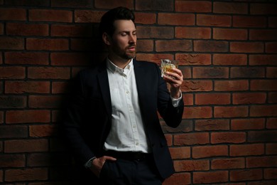 Photo of Man in formal suit holding glass of whiskey near red brick wall