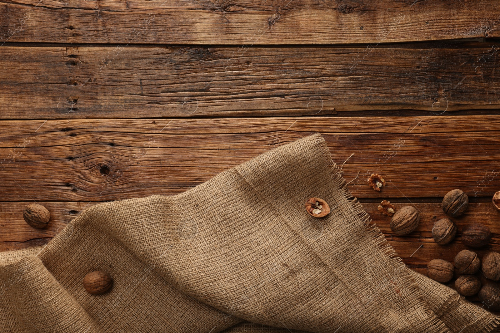 Photo of Burlap fabric and walnuts on wooden table, top view. Space for text