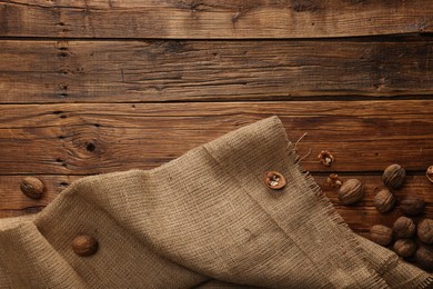 Burlap fabric and walnuts on wooden table, top view. Space for text