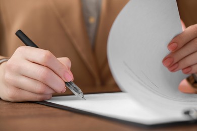Photo of Woman signing documents at wooden table in office, closeup