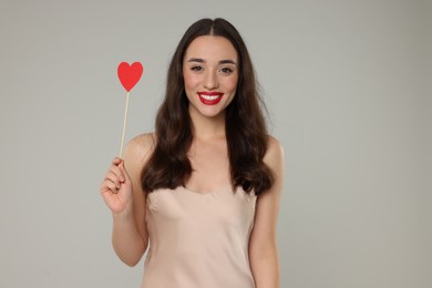 Beautiful young woman with paper heart on grey background