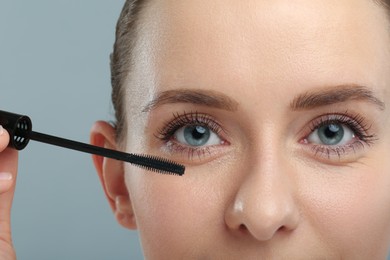 Photo of Woman applying mascara on grey background, closeup