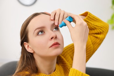Photo of Young woman applying medical eye drops indoors, closeup