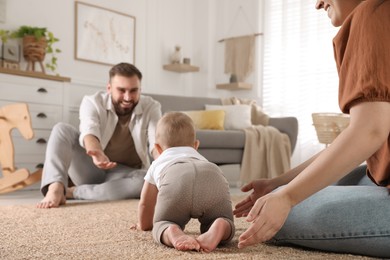 Photo of Happy parents watching their baby crawl on floor at home