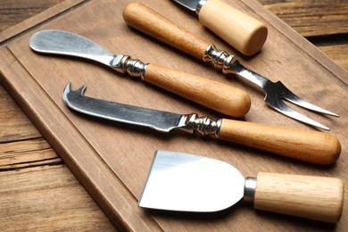 Photo of Cheese knives and fork on wooden table, closeup
