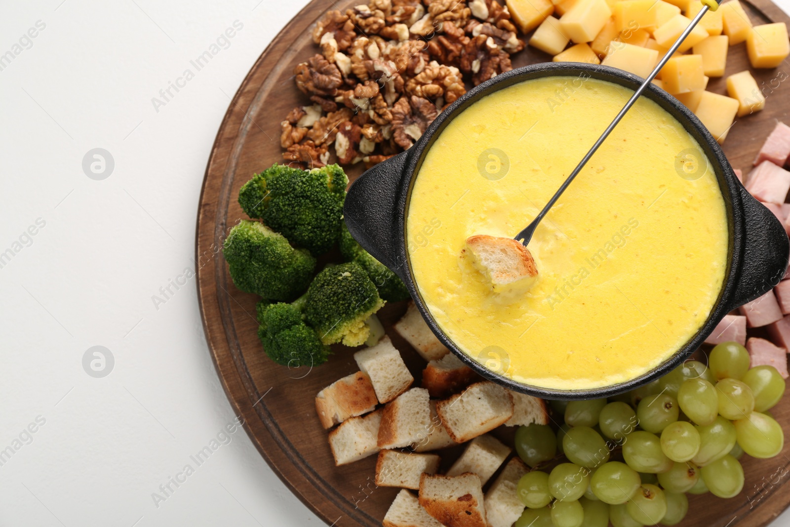 Photo of Fondue with tasty melted cheese, fork and different products on white table, top view