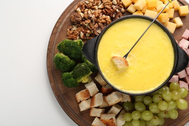 Fondue with tasty melted cheese, fork and different products on white table, top view