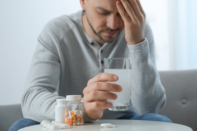 Photo of Man taking medicine for hangover at home, focus on hand with glass