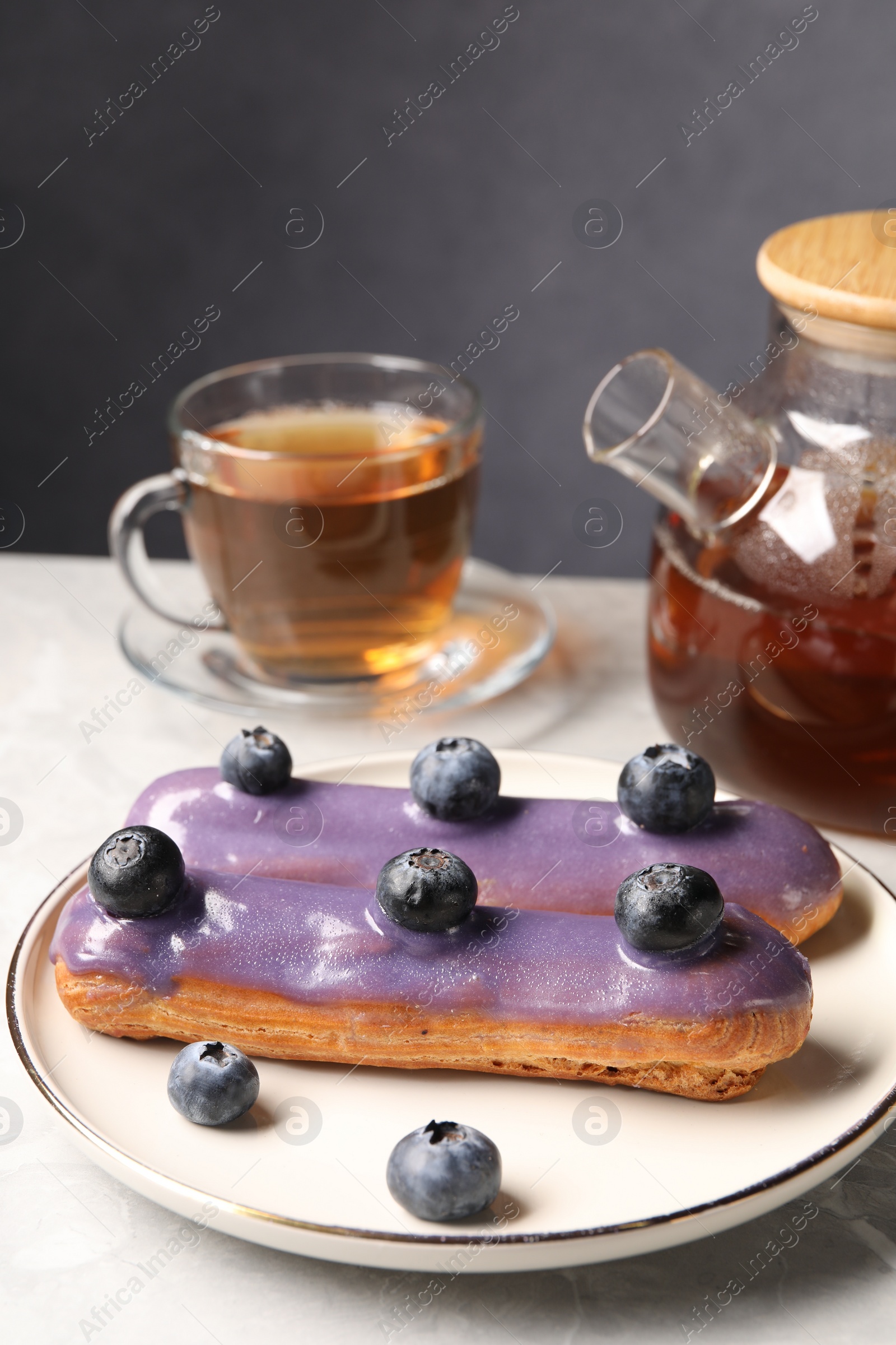 Photo of Tasty glazed eclair with blueberries and tea on grey marble table, closeup