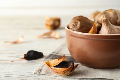 Photo of Bowl and black garlic on white wooden table. Space for text