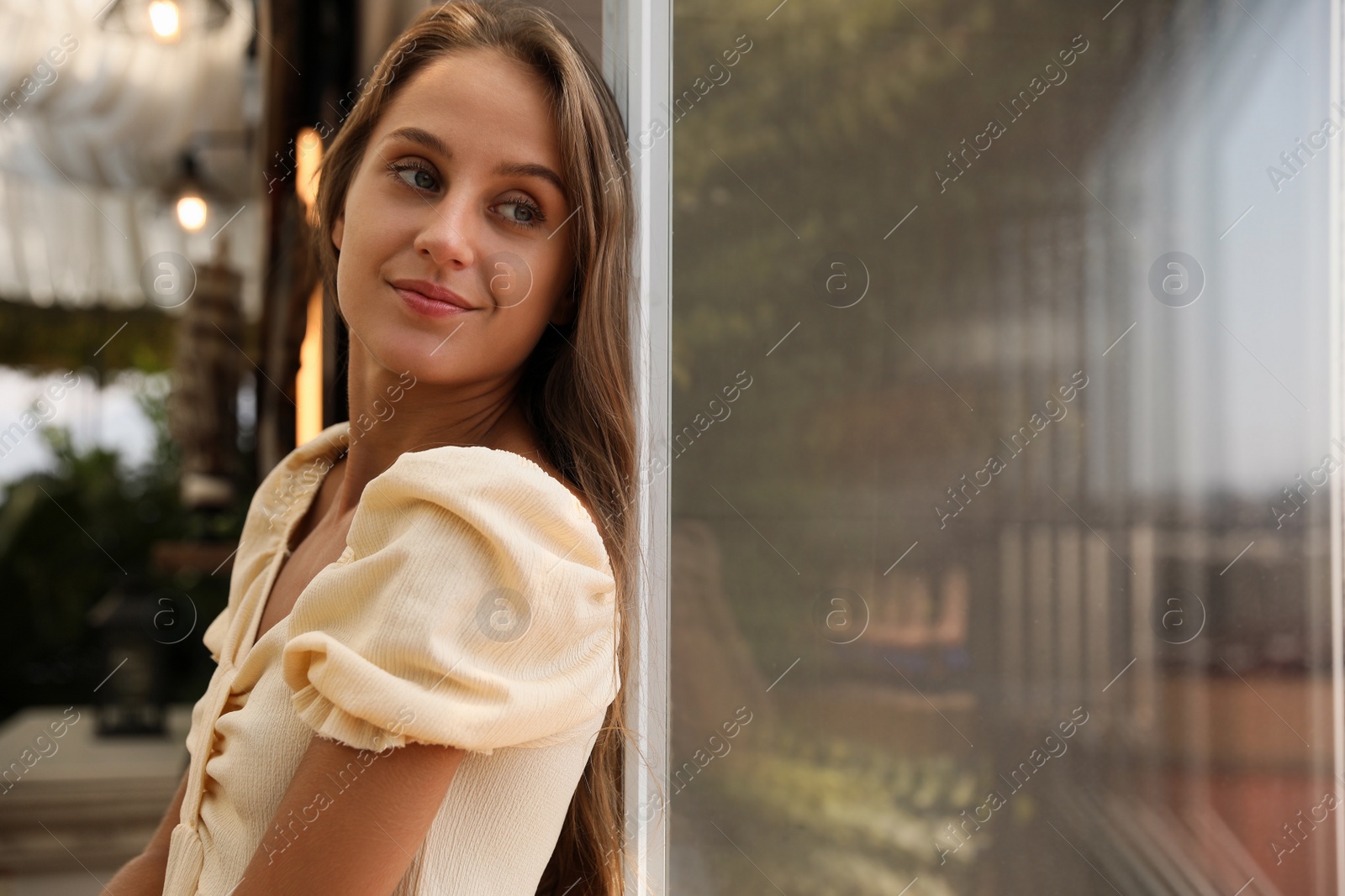 Photo of Beautiful young woman standing on balcony, space for text