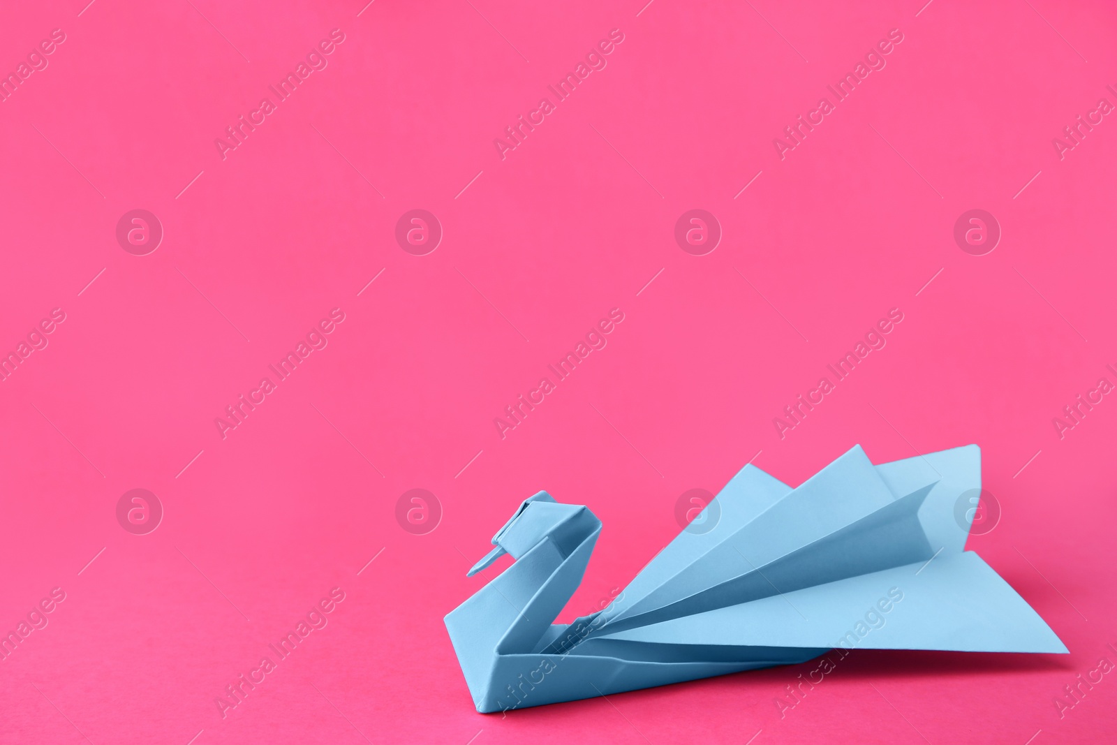 Photo of Light blue paper swan on pink background, space for text. Origami art