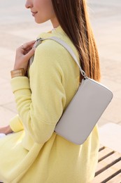 Fashionable young woman with stylish bag on bench outdoors, closeup