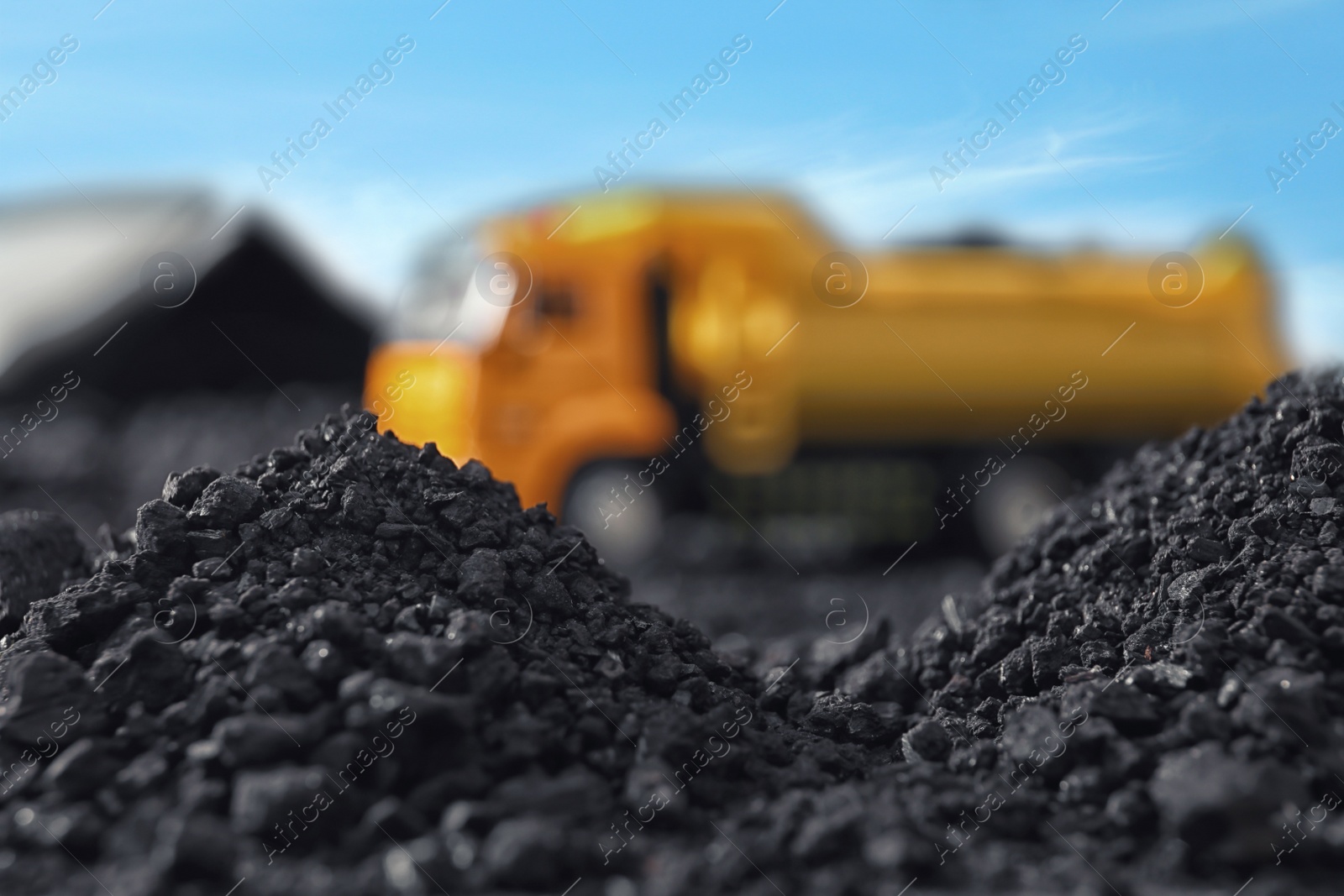 Image of Piles of coal and blurred yellow truck on background, closeup