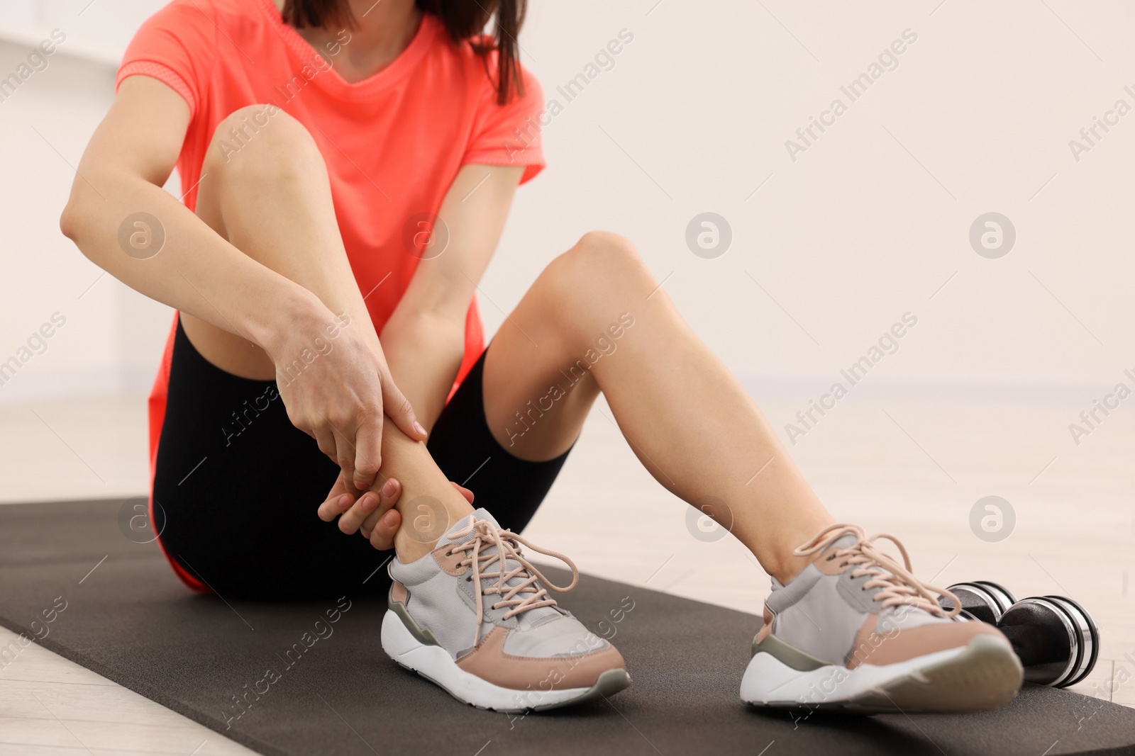 Photo of Woman suffering from leg pain on exercise mat indoors, closeup