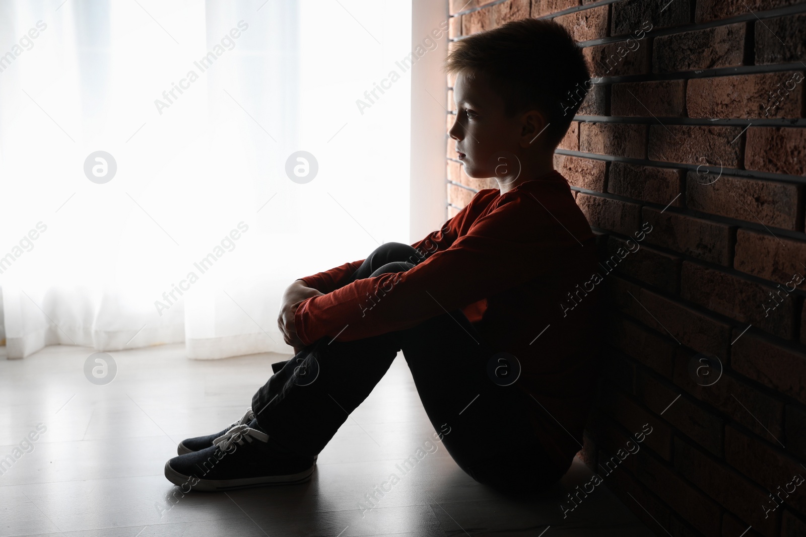 Photo of Sad little boy sitting near brick wall. Domestic violence concept