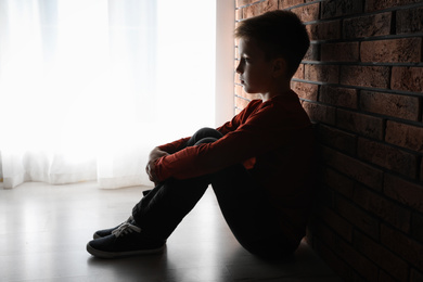 Sad little boy sitting near brick wall. Domestic violence concept