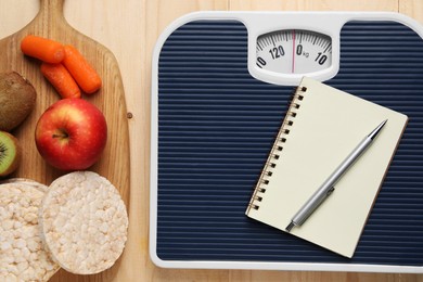 Healthy diet. Scale with notebook and products on wooden table, flat lay