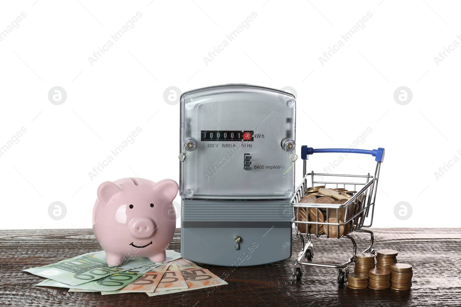 Photo of Electricity meter, piggy bank and small shopping cart with money on wooden table against white background