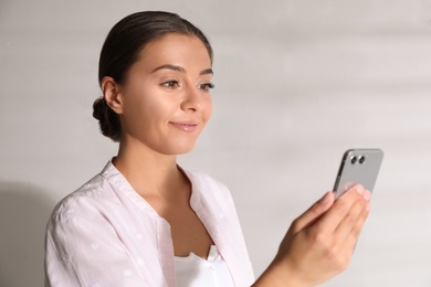 Young woman unlocking smartphone with facial scanner near white wall. Biometric verification