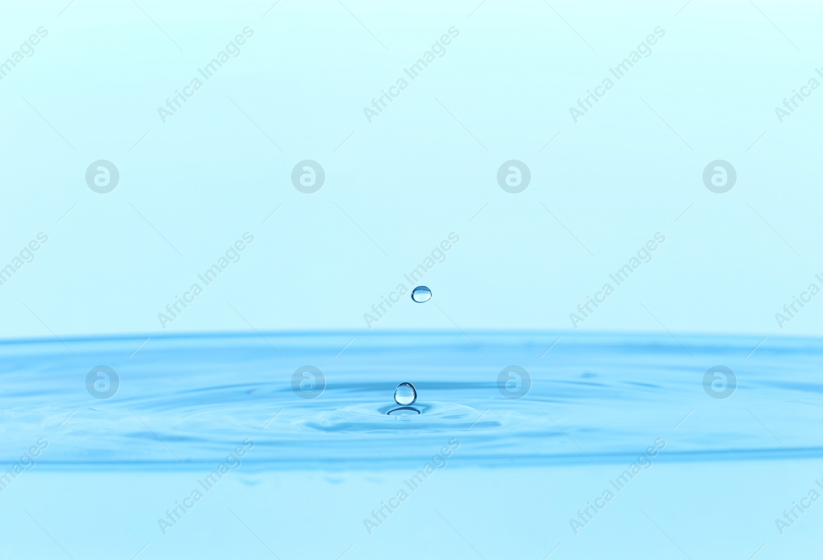 Photo of Drops falling into clear water on light blue background, closeup