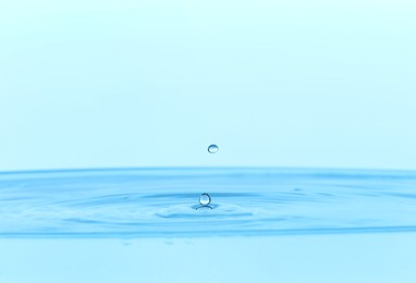 Photo of Drops falling into clear water on light blue background, closeup