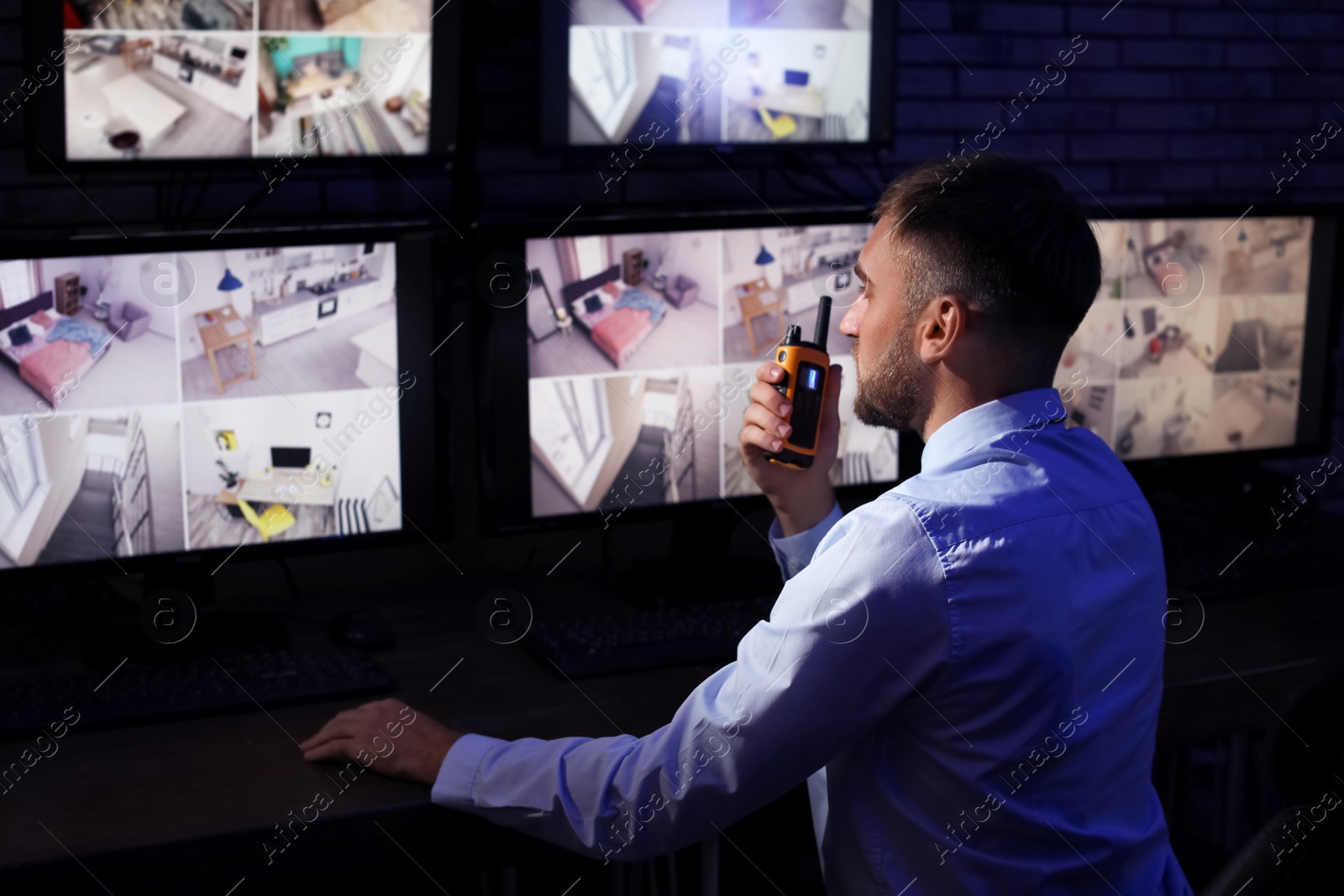 Photo of Male security guard with portable transmitter monitoring home cameras indoors at night