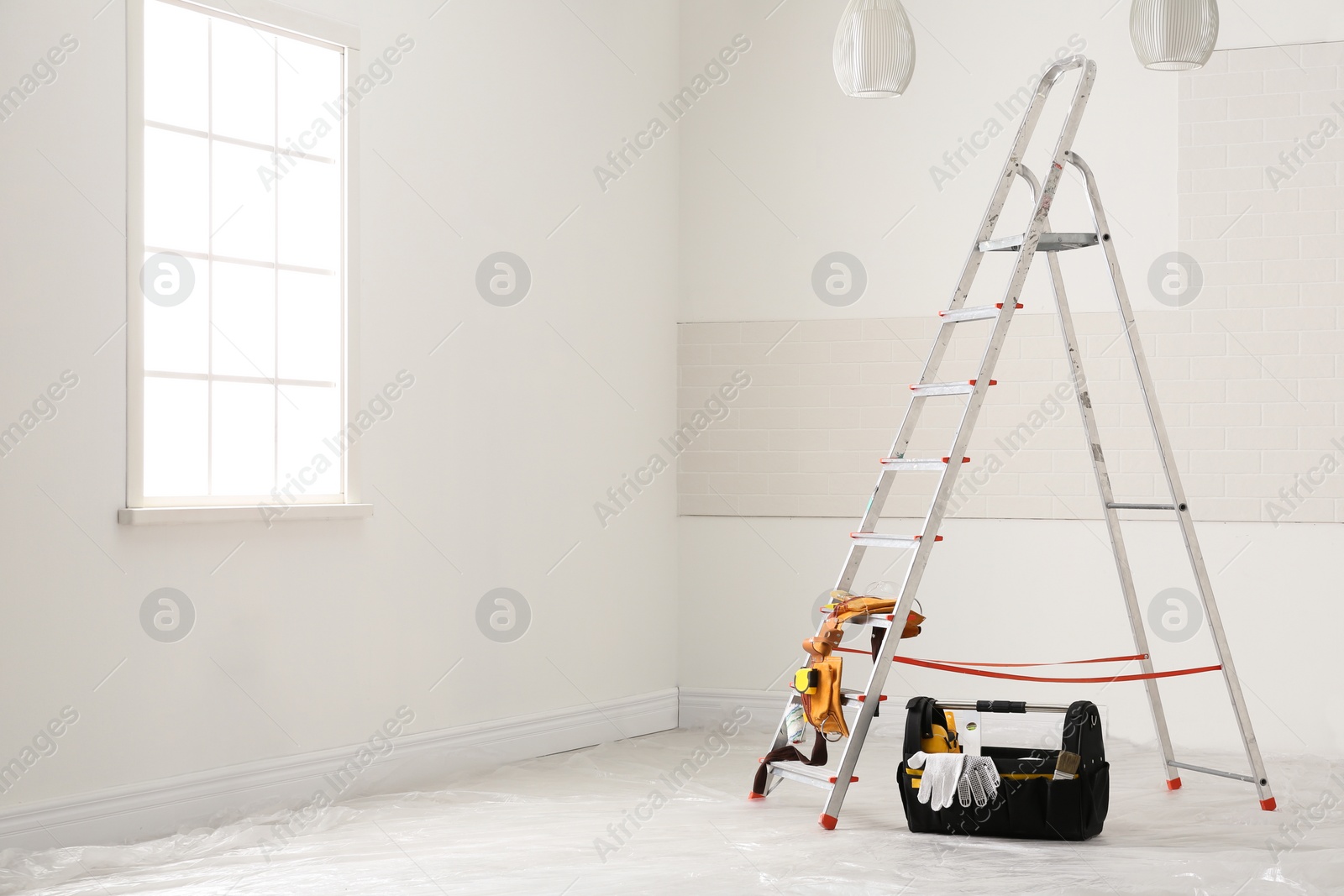 Photo of Stepladder and different tools near wall in room. Interior renovation