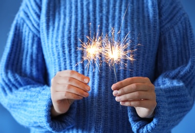 Photo of Woman holding burning sparklers on blue background, closeup