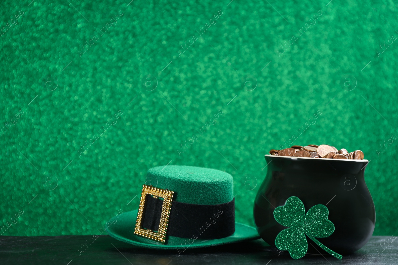 Photo of Pot of gold coins, hat and clover on black stone table against green background, space for text. St. Patrick's Day celebration