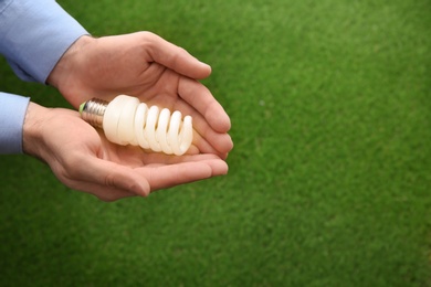 Photo of Man holding energy saving bulb for lamp over green grass, closeup. Space for text