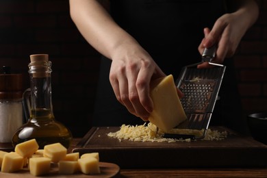 Woman grating cheese at wooden table, closeup