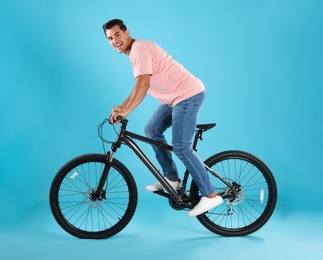 Photo of Handsome young man with modern bicycle on light blue background