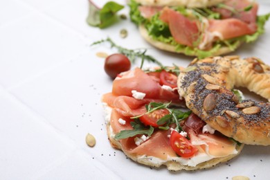 Photo of Tasty bagel with cured ham, cheese, tomatoes and arugula on white tiled table, closeup. Space for text